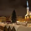 Рождественская ярмарка на заснеженной Ратушной площади Таллина ночью, в центре — большая ель