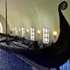 Осебергский корабль викингов с высоким завитым носом в светлом сводчатом зале Музея кораблей викингов в Осло